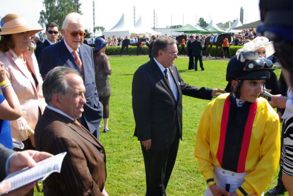 Das Gestüt Auenquelle im Derby-Führring 2013: Das Besitzerpaar Peter-Michael und Helga Endres (im Hintergrund links), Karl-Dieter Ellerbracke (Mitte), Trainer Mario Hofer (vorne links) und Jockey Andrea Atzeni. Der chancenreiche Starter Global Bang wurde damals Fünfter. www.dequia.de